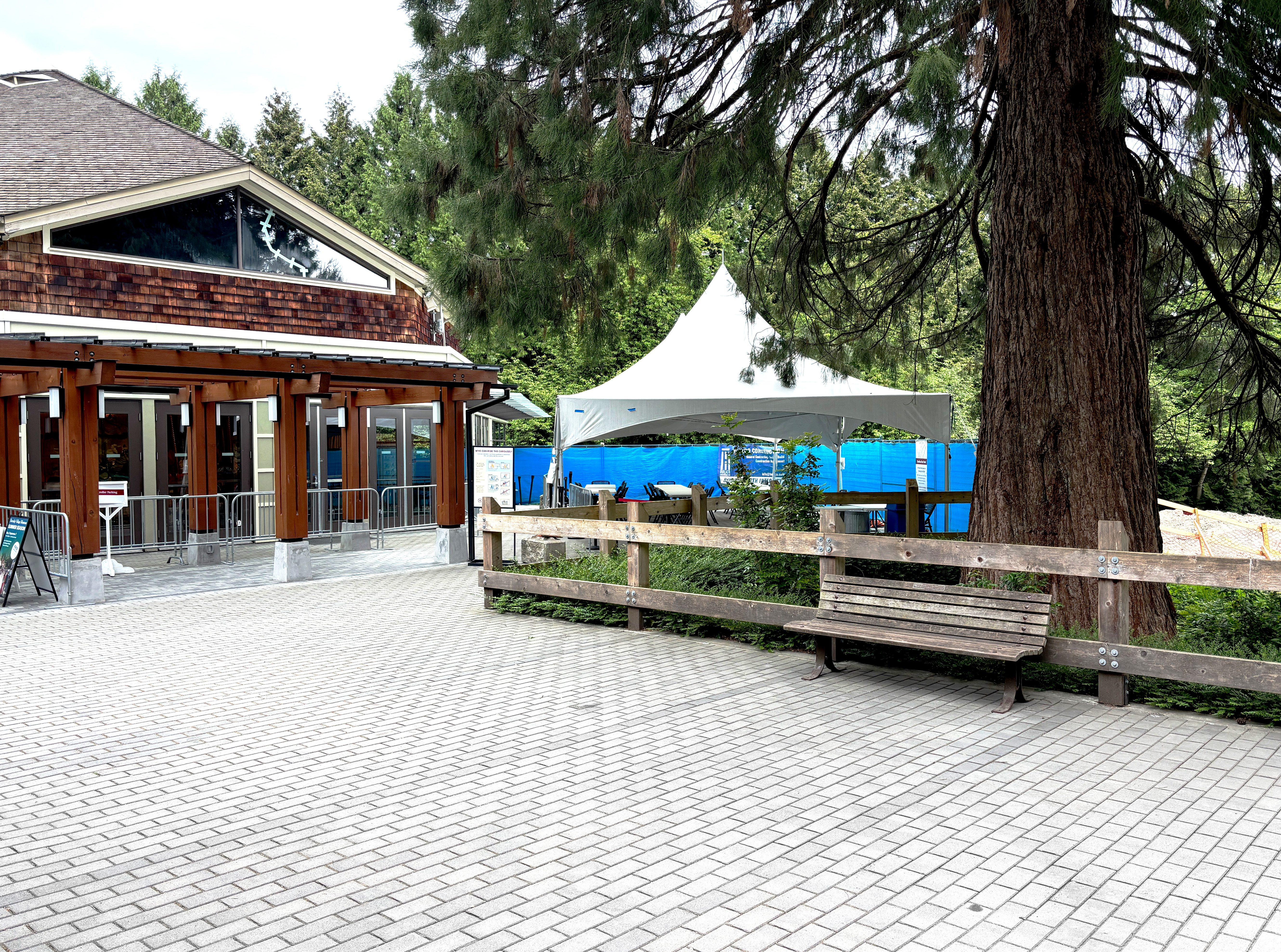Outdoor plaza with a building, white event tent, benches, and trees.